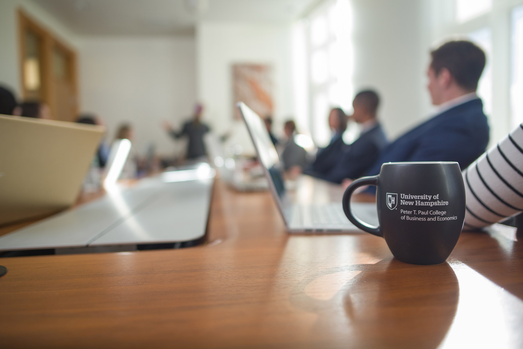 A coffee mug with the Peter T. Paul College of Business and Economics logo designed on the front in a business meeting room