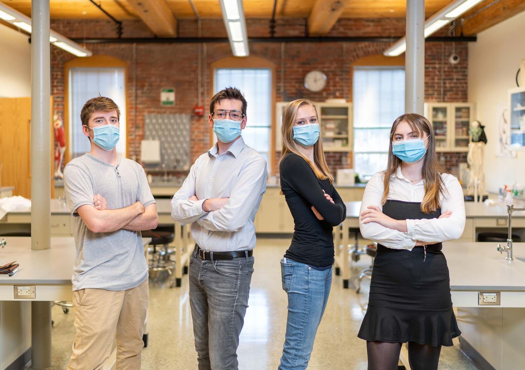 Manchester's NoMADS team members wearing masks and fancy clothes with crossed arms in a laboratory