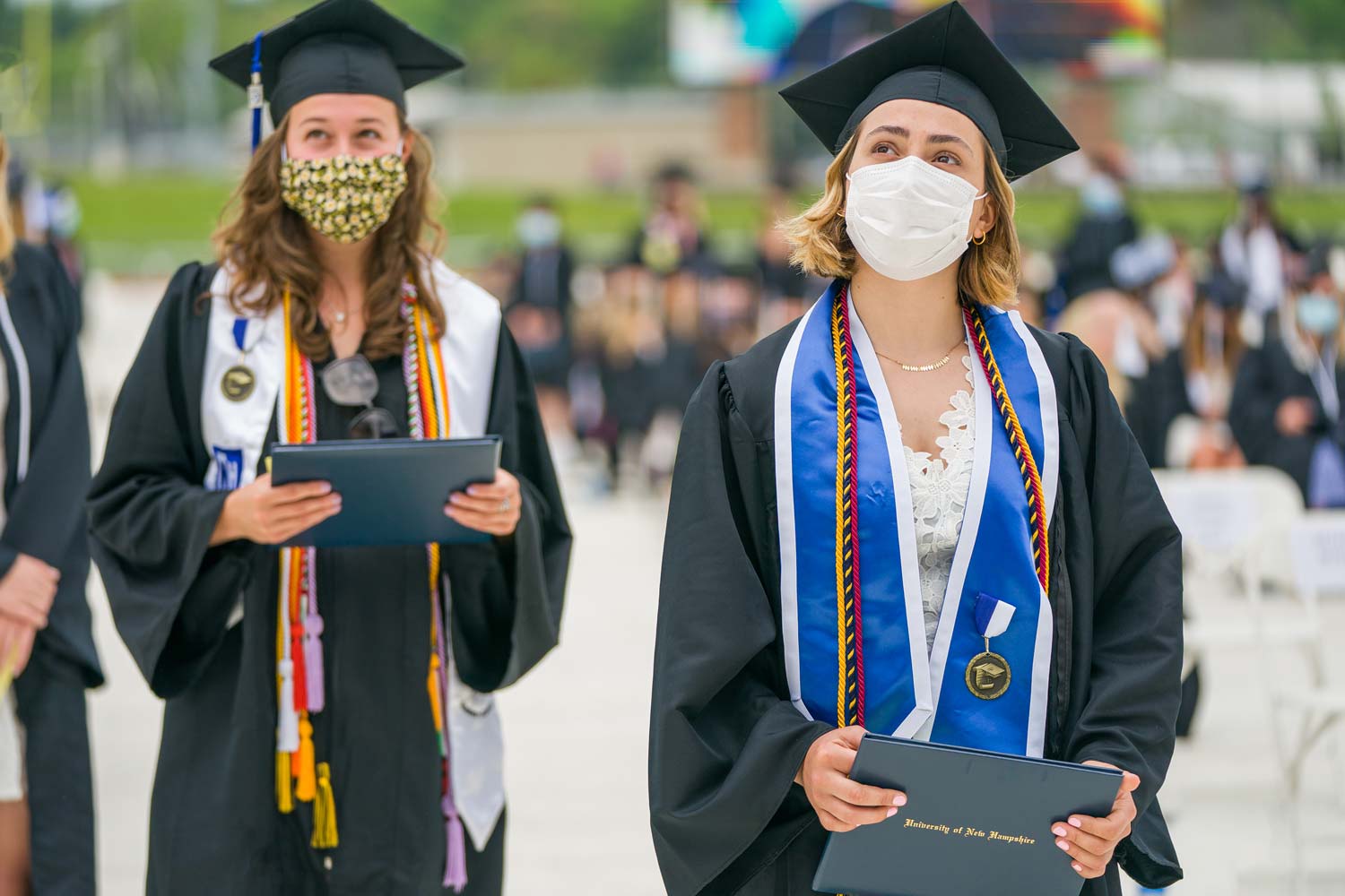 Two students in caps and gowns walk by with their diplomas in hardcover booklets