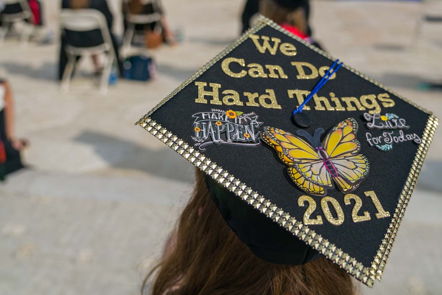 A graduation cap that reads "we can do hard things" in gold lettering with a butterfly and motivational stickers