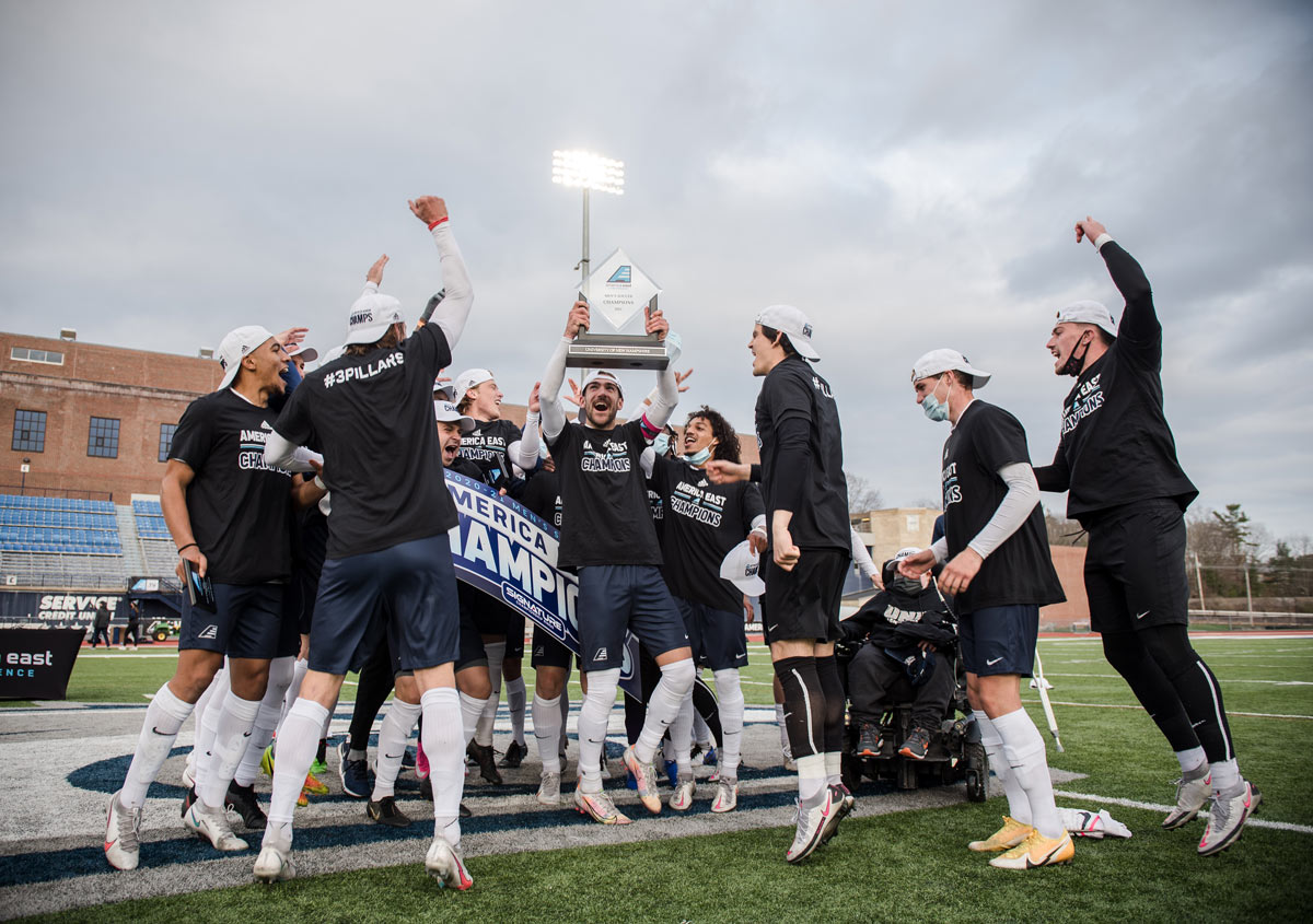 UNH Men's Soccer team celebrating with their trophy