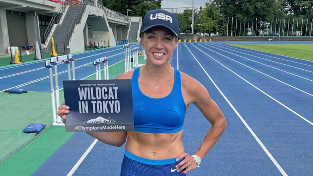 Elle Purrier St. Pierre on the track, wearing her track attire and holding a sign that reads "Wildcat in Tokyo"