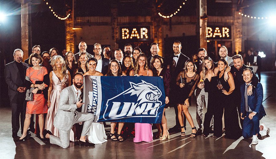 Kellen Millard and Ben Bunker ’03 gathered with family and friends holding a UNH flag