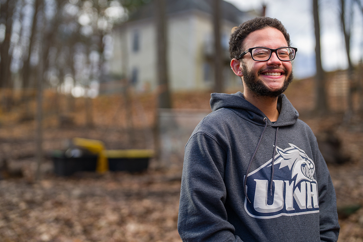 Bryson Badeau ’22 in the woods wearing a UNH alumni hooded sweatshirt
