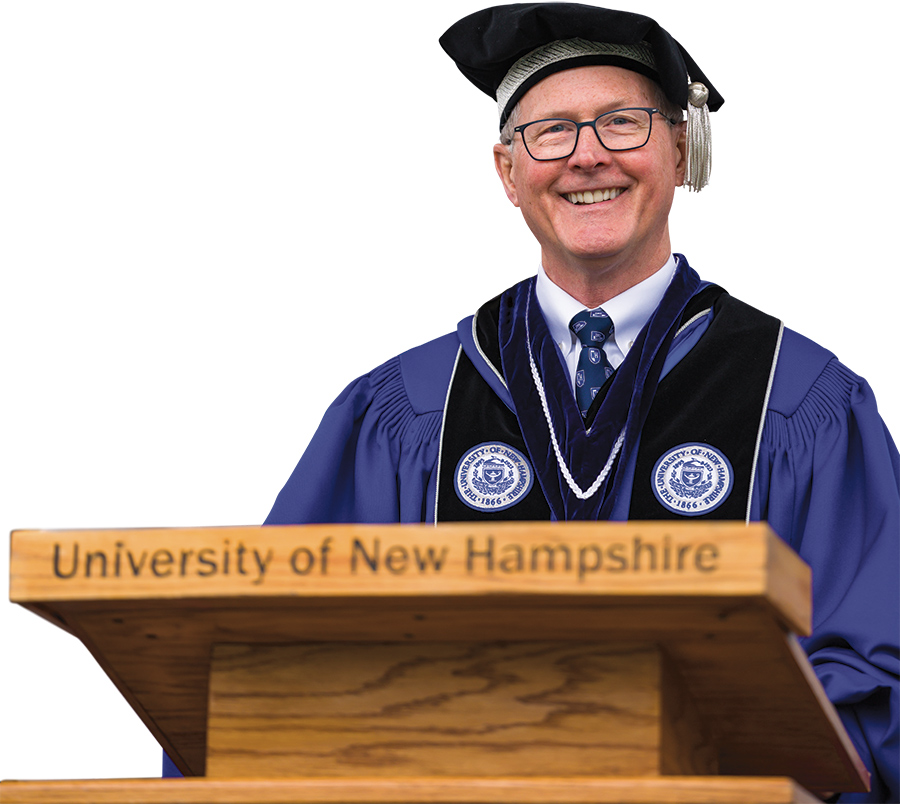 UNH President James W. Dean Jr. smiles in his Commencement cap and gown outfit while standing behind the podium