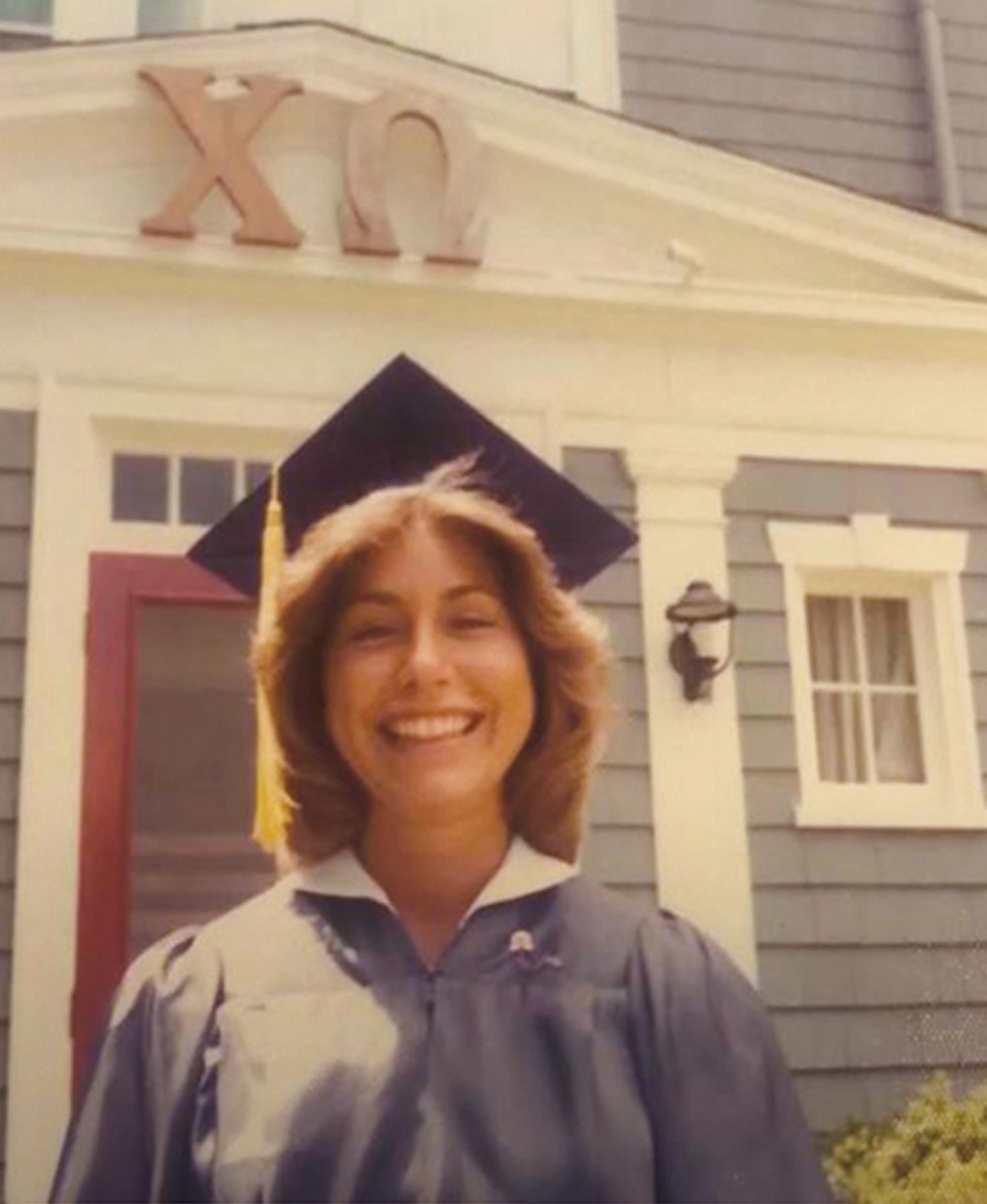 Jude Blake in cap and gown in 1977 in front of her sorority house