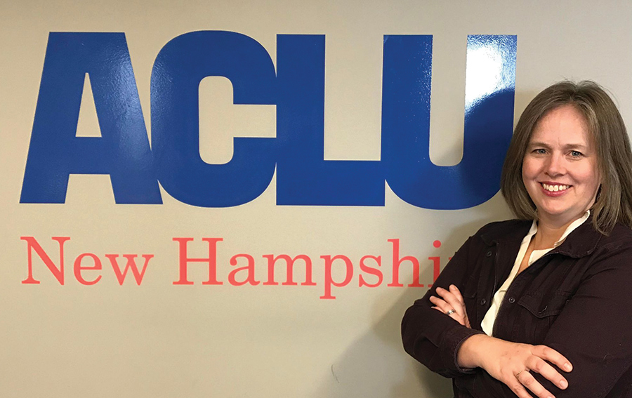 A picture of Heather Holt Totty posing by a wall that says ACLU New Hampshire