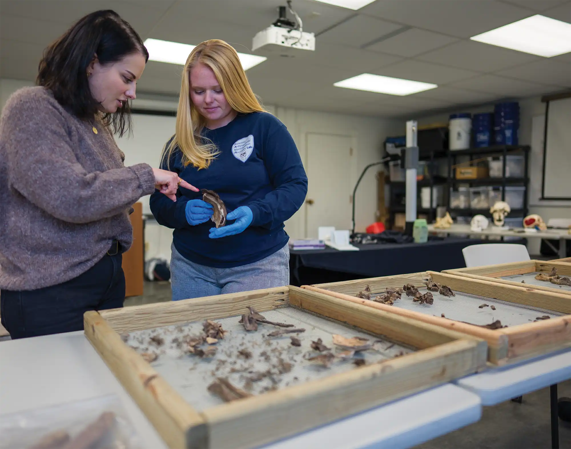 Amy Michael, left, talks with Kylee Jedraszek ’23, while Kylee works with remains discovered that are likely part of a burial area on a poor farm, common in New England in the 1800s and early 1900s. 