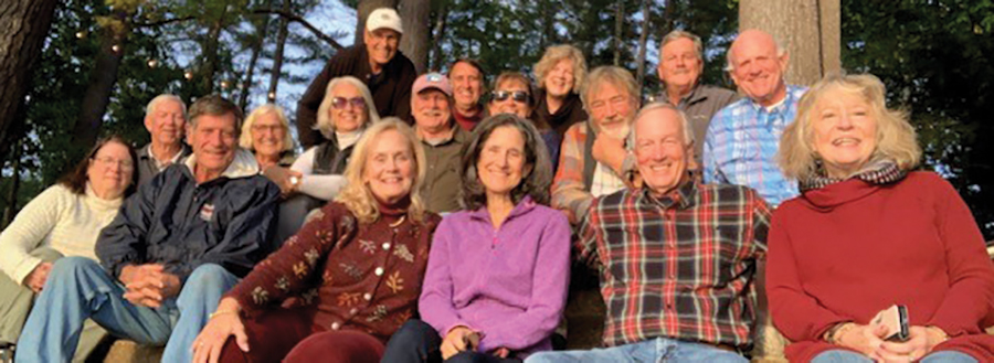 A landscape photograph of Ann Dillon ’75 and husband Bill hosting a fall gathering at their lakeside camp on a chilly September eve outdoors in the forest. In attendance were friends from UNH and Freshman Camp from the class of ’75 and more as they all smile and pose for a picture bunched up together. “We are calling it our first annual Senior Camp!” she says. Top row, left to right: Bill Dillon, Gary Fincke ’75, Ann Donoghue Dillon ’75 ’98G, Gary Dionne ’75; middle row: Bob Murphy ’74, Gayle Murphy ’75, Martha Byam ’75, Paul “Tank” Tanklefsky ’75, Lissa Bedor Smart ’75, Wayne King ’77, Bob Eames ’75; front row: Catherine Eames, Glenn Smart ’77, Jan O’Connor, Gay Tanklefsky, Dave O’Connor ’75, Marcia Grant Dionne.