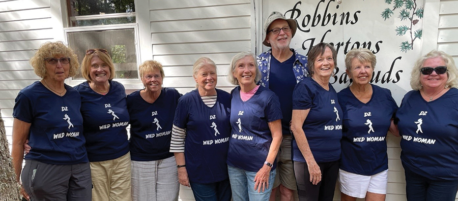 A landscape photograph of Jude Robbins Bagrud ’66 hosting friends at her Little Moussam Lake house in Shapleigh Maine, back in August. From left are Kathy Gerbracht Hall ’66, Cathy Corbett, Sue Hatt Conner ’66, Betty Blesedell Crepeau ’66, ’88G, ’94PhD, Sandra Chadwick Pinkham ’66, Meryl Johnson Roy ’66, Lynda “Boo” Anderson Rishkofski ’68, Judy Robbins Bagrud ’66, and in rear is Jack O’Malley ’66 known back then as the DZ houseboy but he was the best friend to all of them as they all smile and pose for a picture together outside on the side of the lake house