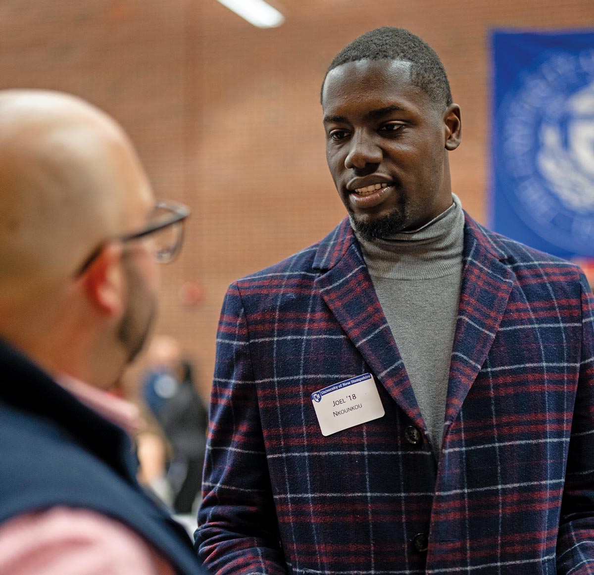 Alumni Board member Joël Nkounkou wears a red and navy plaid suit and speaks to Shersingh Joseph Tumber-Dávila ’15PhD who stands in the foreground