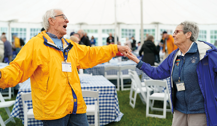Two UNH alumni elderly individuals (a man and a woman) glance at each other as they hold hands and dance together enjoying a good time