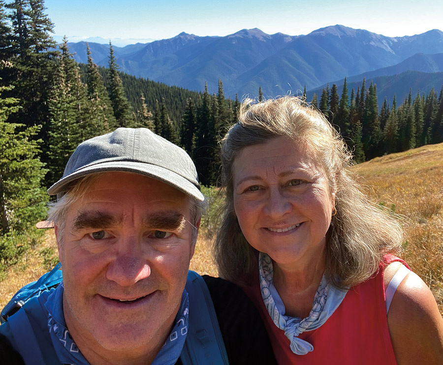 Doug Lenz ’79G (in a grey cap and blue bandana around neck with a blue backpack) with wife Karin (in a red top and light blue bandana around her neck) in Olympic National Park, Washington on a sunny bright day.