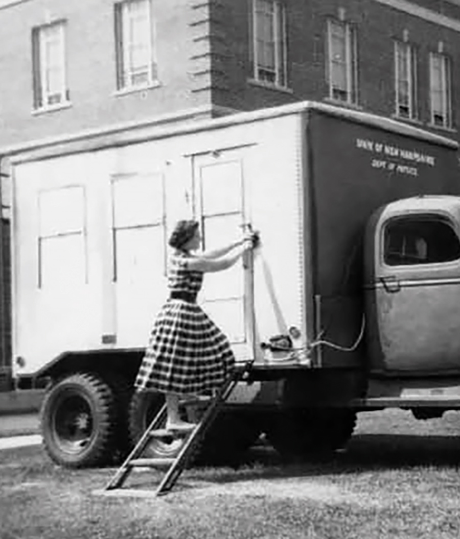 Black & white photograph of Peggy Ann Shea ’58 in a dress at the Neutron Monitor Truck parked behind DeMeritt Hall building. “I used that picture in several of my ‘historical’ lectures.”
