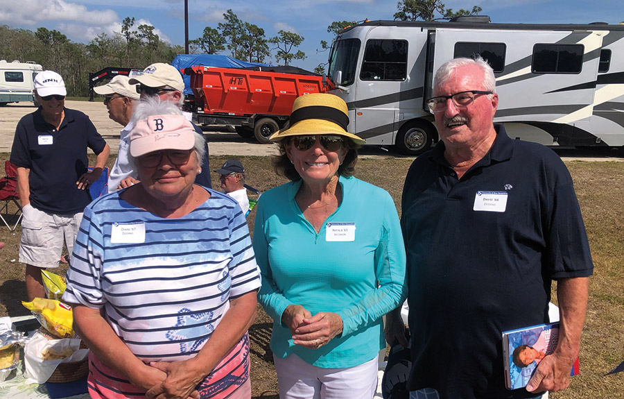Dave ’66 (right with dark navy blue polo top and prescription see through black outer frame glasses) and Di Deering ’67 (left with pink visor cap and blue/white/red striped themed shirt) stand next to Natalie Salatich Jacobson ’65 (middle with sunglasses, blue jacket and tan/black colored sun hat) at the Southwest Florida alumni chapter annual Red Sox game.