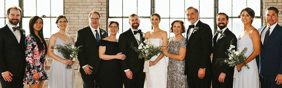 Bernard Roy ’77 and wife Kim celebrate one of their daughter’s wedding as they all smile and pose next to each other in their wedding apparel.