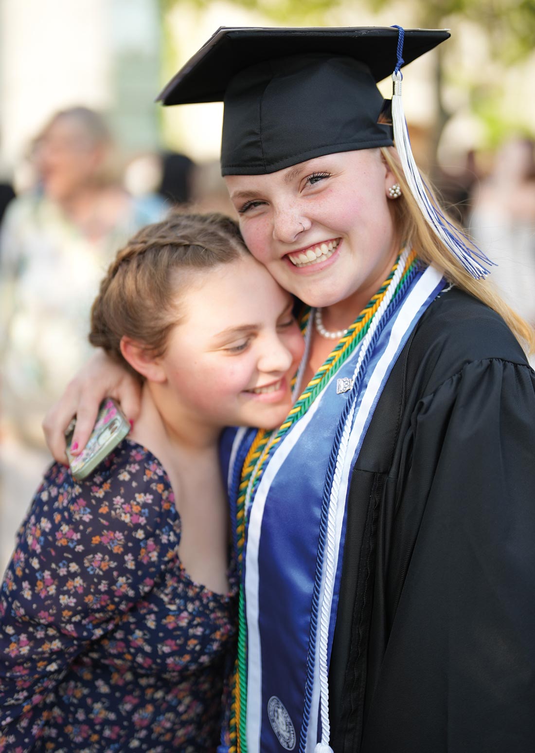 a blonde young woman in a cap and gown holds a similar looking young girl in a tight embrace, both smiling
