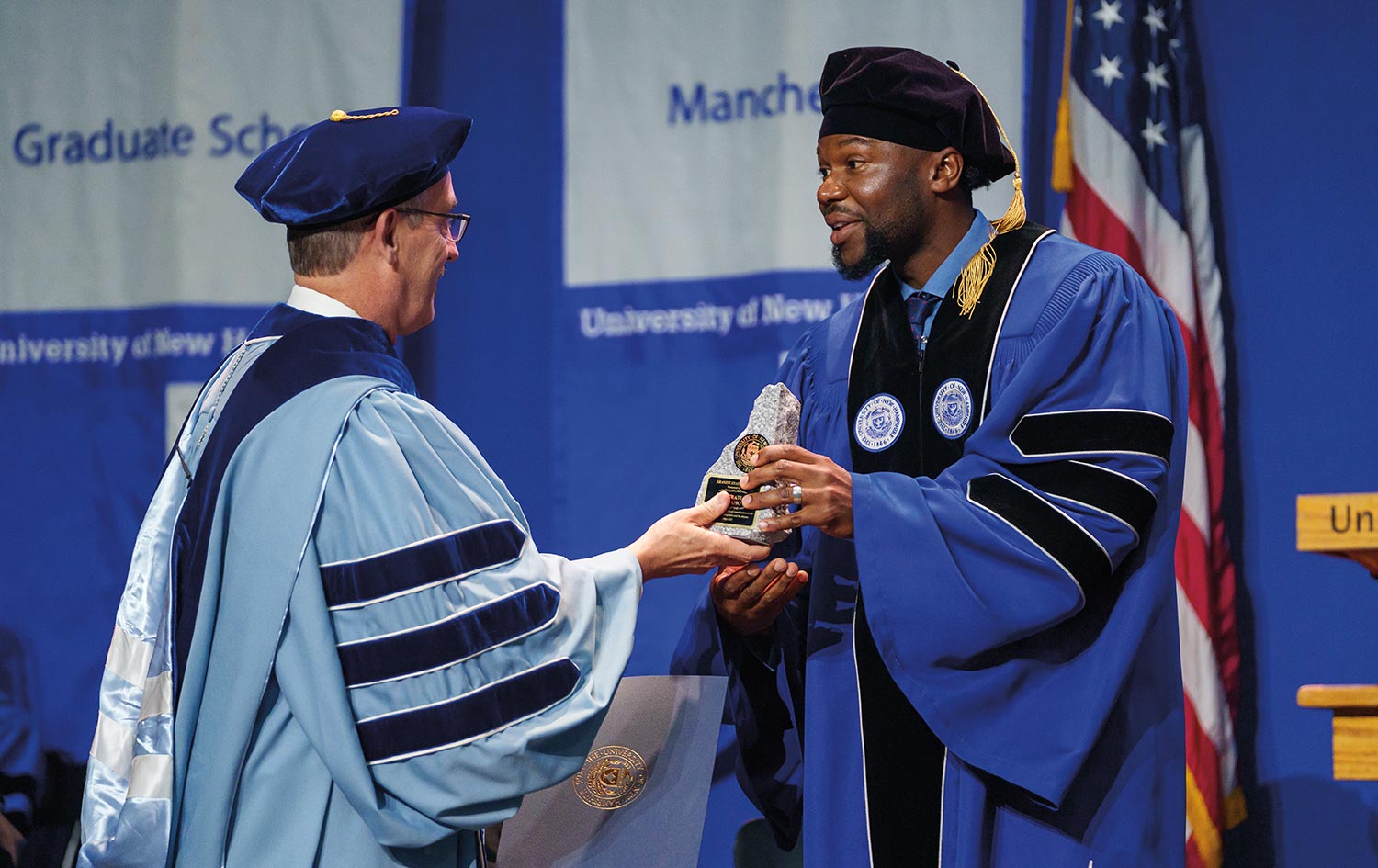 on stage a faculty member presents Deo Mwano with the Granite State Award