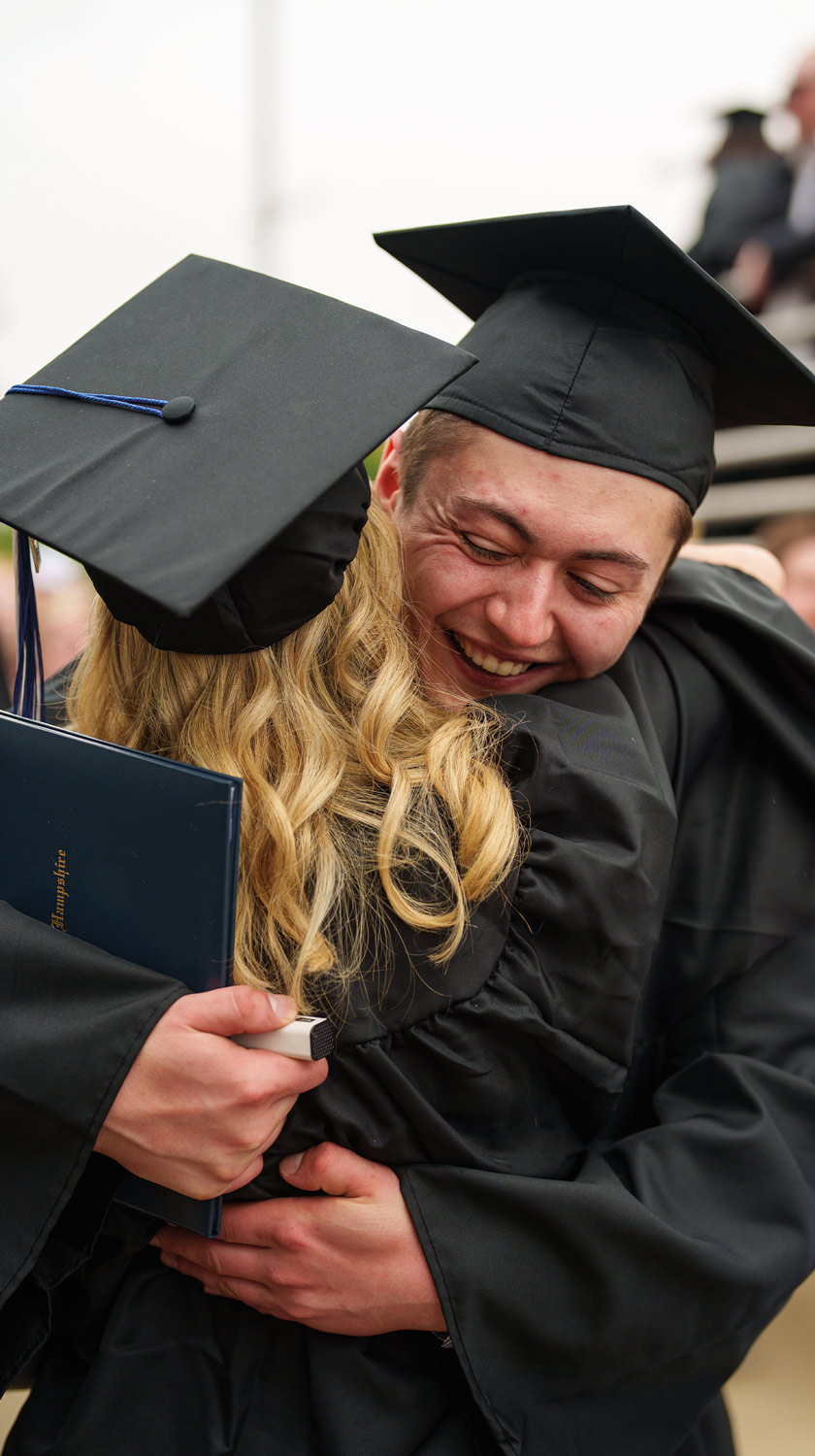 a man in a cap and gown smiles while hugging a woman in a cap and gown