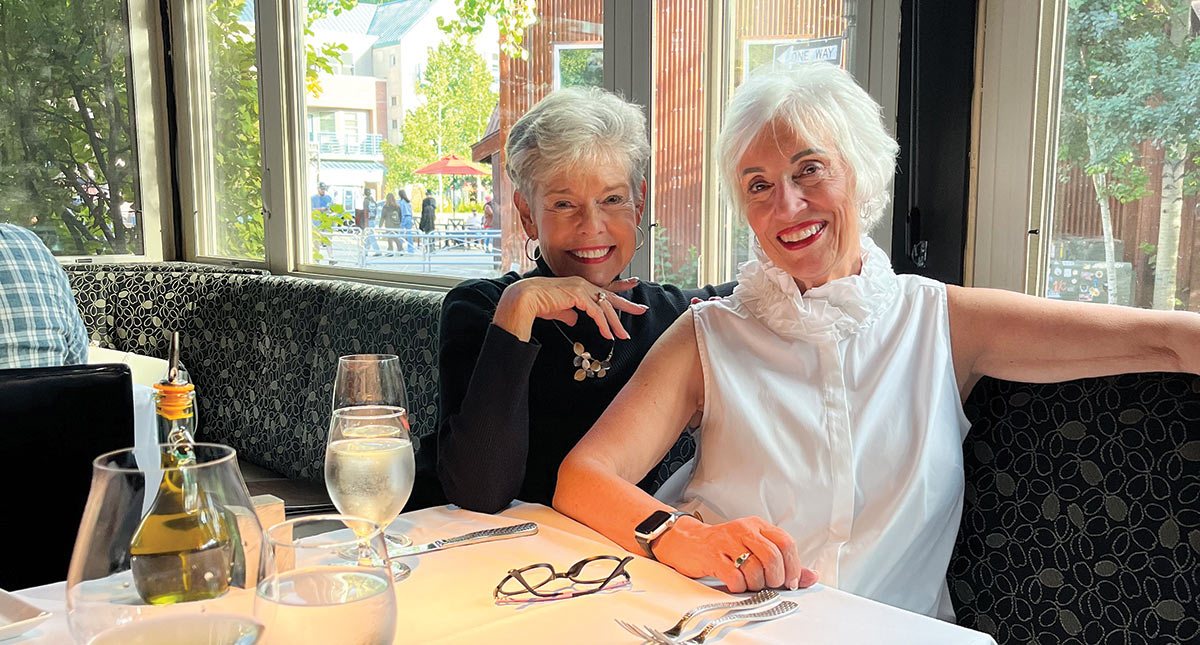 Two women, one in a black shirt and one in a white shirt, sitting in a restaurant smiling for a picture