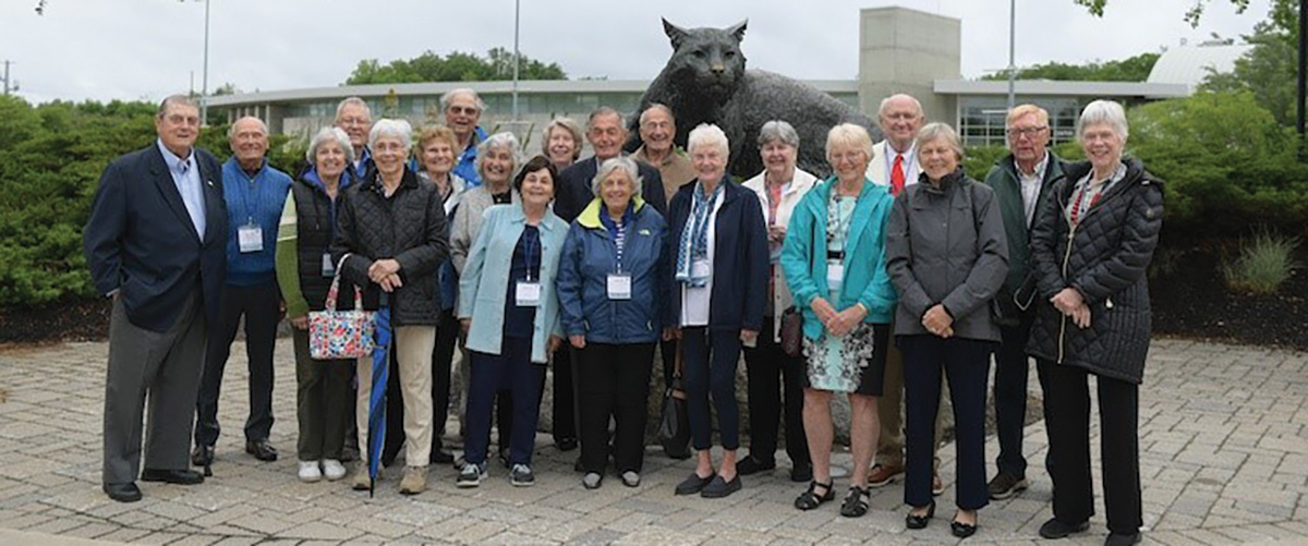 Group of people posing in front of a large statue of a bobcat