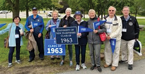 8 people standing side by side, the one in the middle holding a sign for the class of 1963