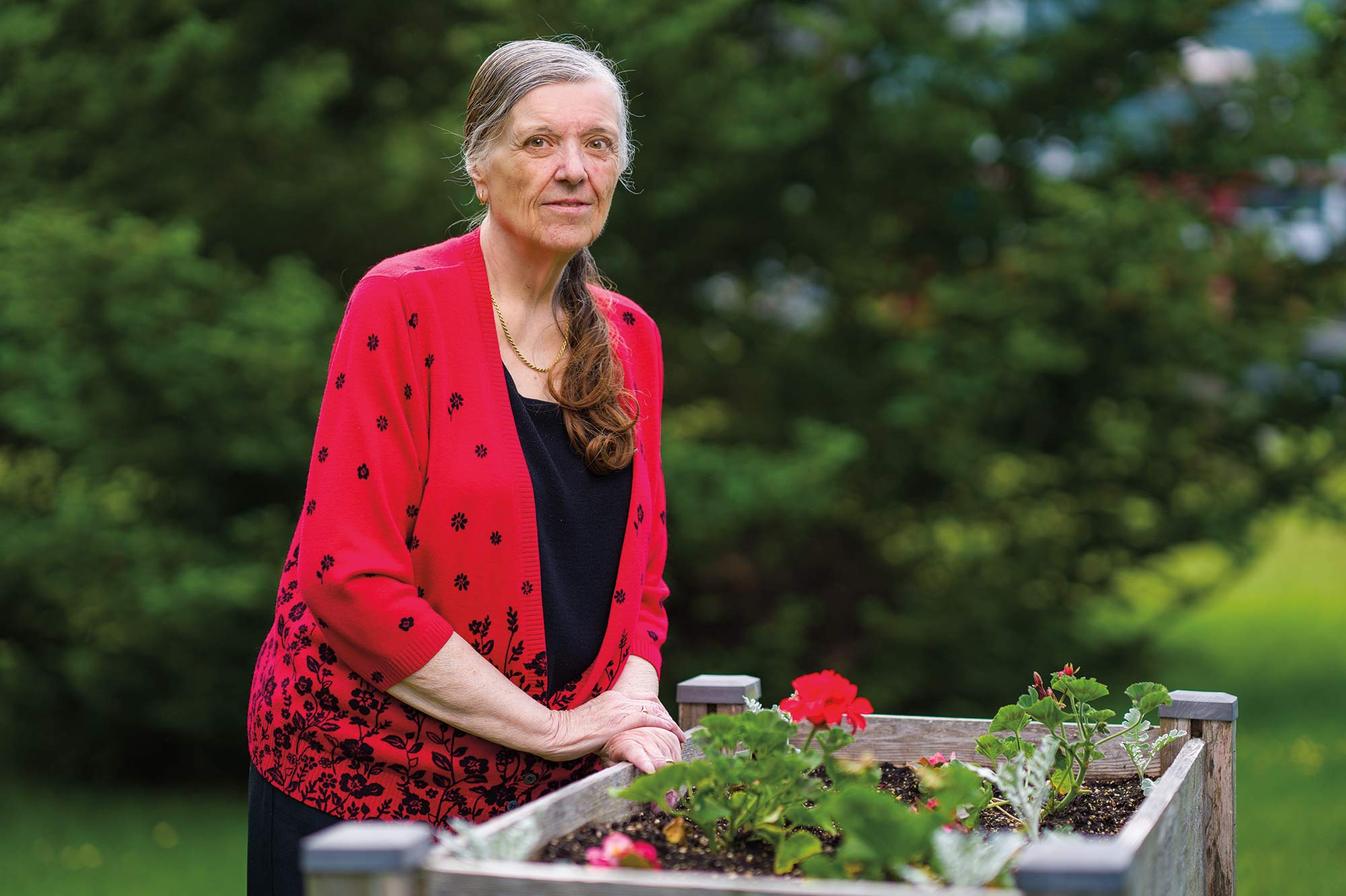 Colette Helene in a red sweater over a black shirt, standing over a raised garden bed