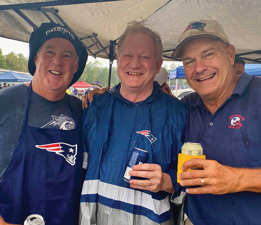Close-up portrait photograph of Kappa Sigma brothers Ned Burke ’83, Jim Freeman ’84 and Bobby Coppins ’83 all dressed up in New England Patriots team gear of some sort as they all are standing underneath a tent outside somewhere