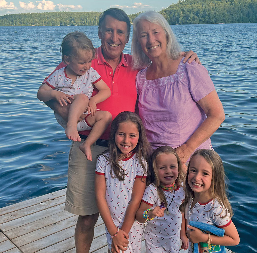 Portrait close-up photograph of Martha Byam ’75 with her husband and four grandchildren out somewhere on a wooden platform deck out at the lake in Squam