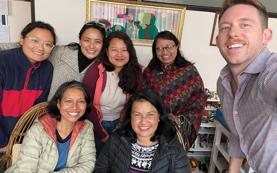 Landscape photograph of class correspondent Ryan Walls ’03 with therapists from the Nepal Youth Foundation child counseling center when he visited in February 2023; the center is the first of its kind in Nepal. They all are smiling for a group photo next to each other.