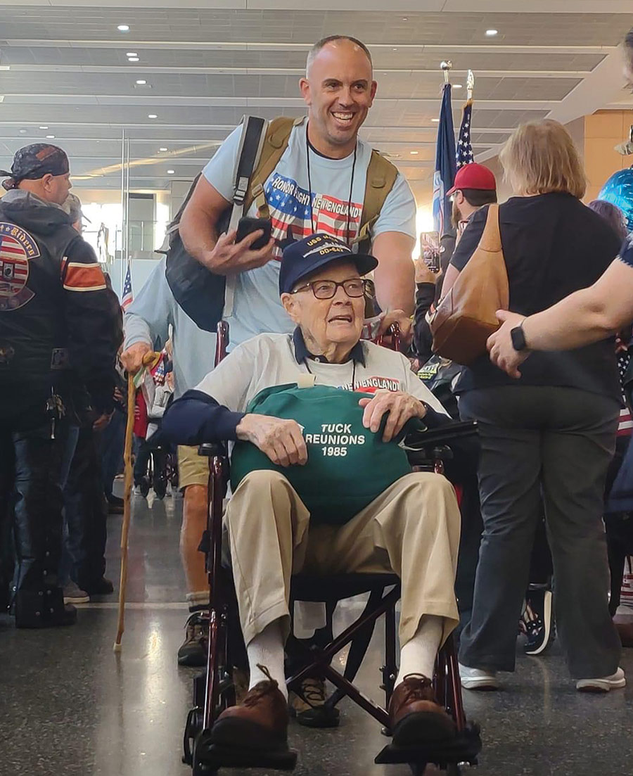 Close-up portrait photograph of John Jeanson ’05 taking part in a recent Honor Flight New England trip to DC with veterans as he assists to push a veteran individual in a wheelchair. (photo courtesy of Honor Flight New England)