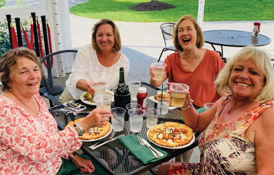 Landscape photograph of Dawn Kimball ’77 having a wonderful lunch with, left to right, Polly Gazaway Stanwood ’77, Sandra Fanny Ziegra ’79 and Carol Gulla ’76 outside somewhere at a patio table