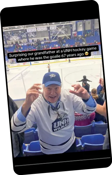 Elderly man in a UNH Wildcats jersey and cap smiling and cheering in the stands at a hockey game, with text overlay reading “Surprising our grandfather at a UNH hockey game where he was the goalie 67 years ago.”