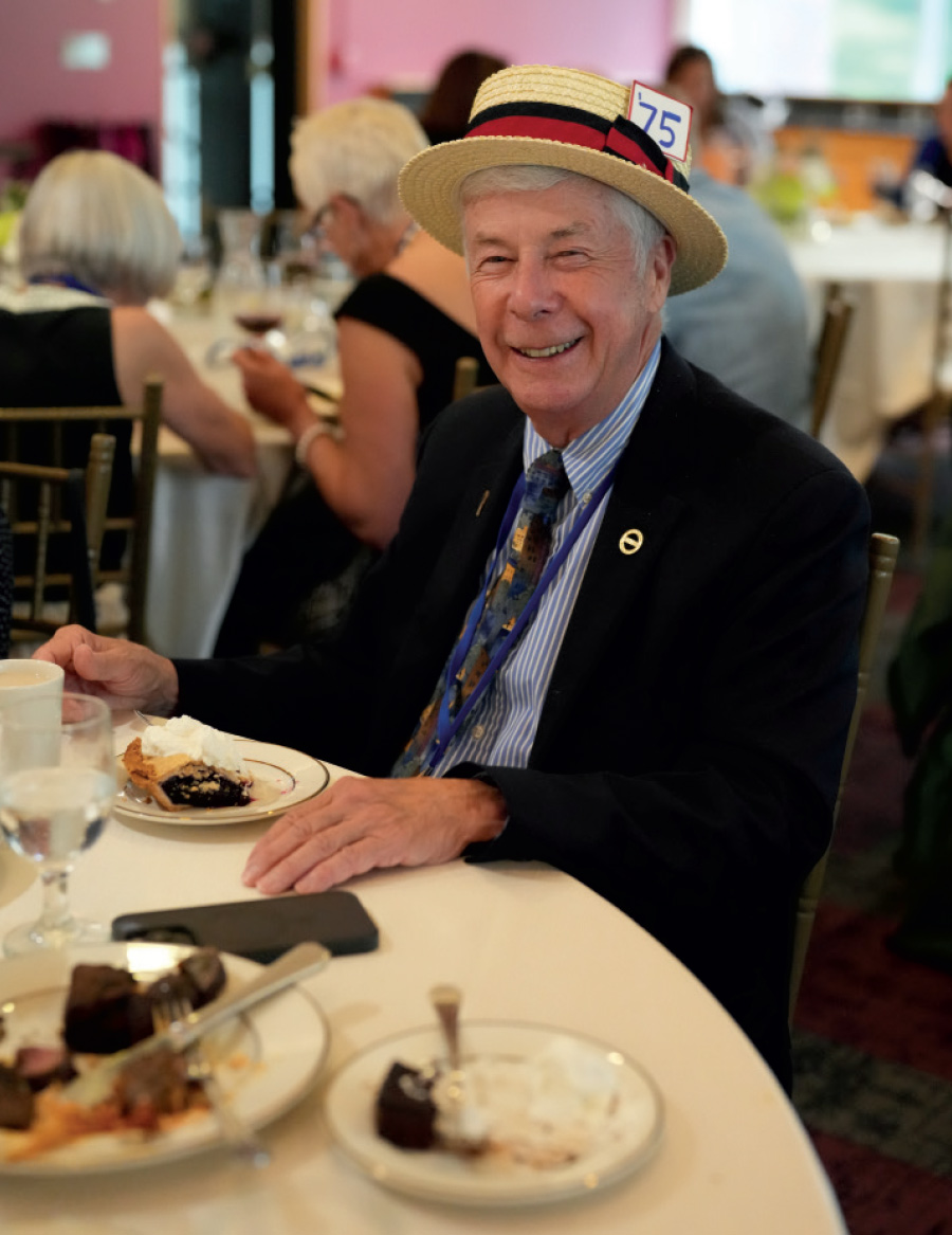 older gentleman wearing straw hat with number 75 on it while sitting at a table