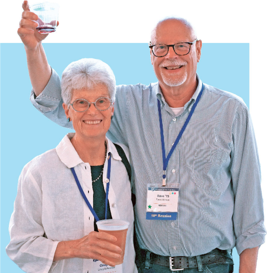 man holding glass cup in the air while woman is next to him under his arm, both smiling