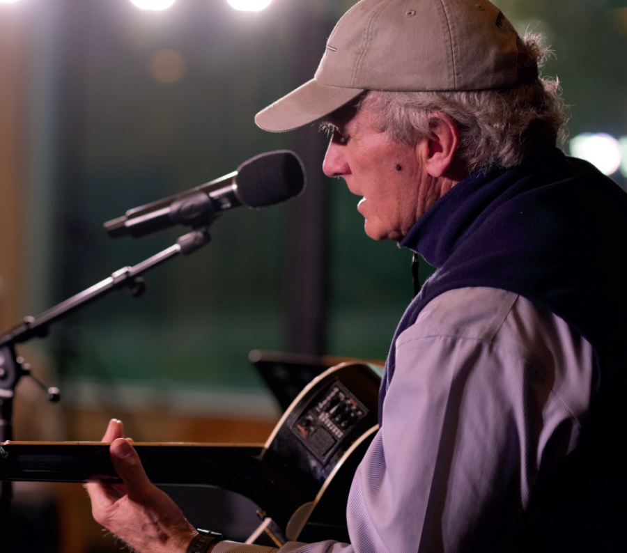 man in hat, button up, and vest playing acoustic guitar