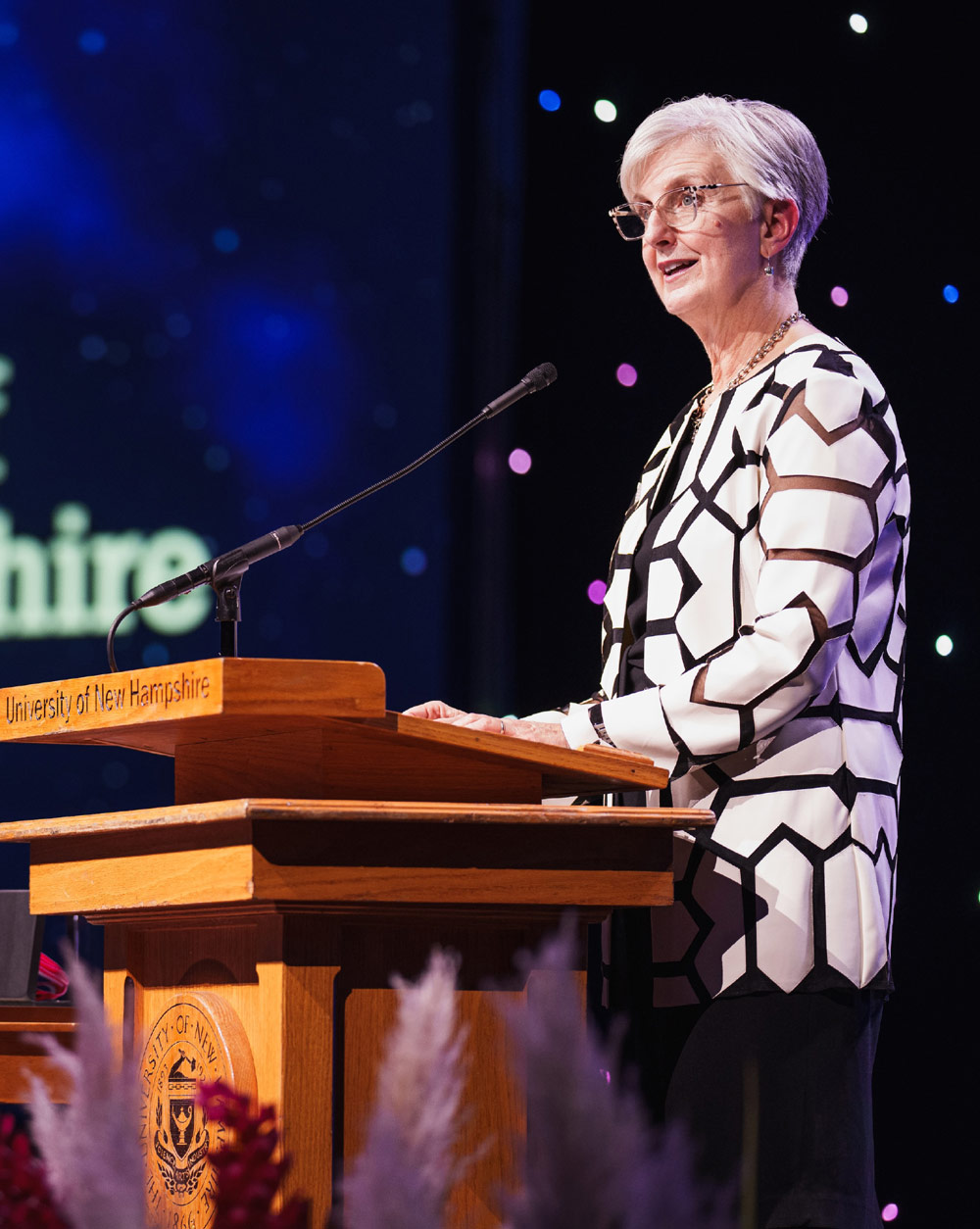 A person speaking at a podium with a University of New Hampshire seal and text.