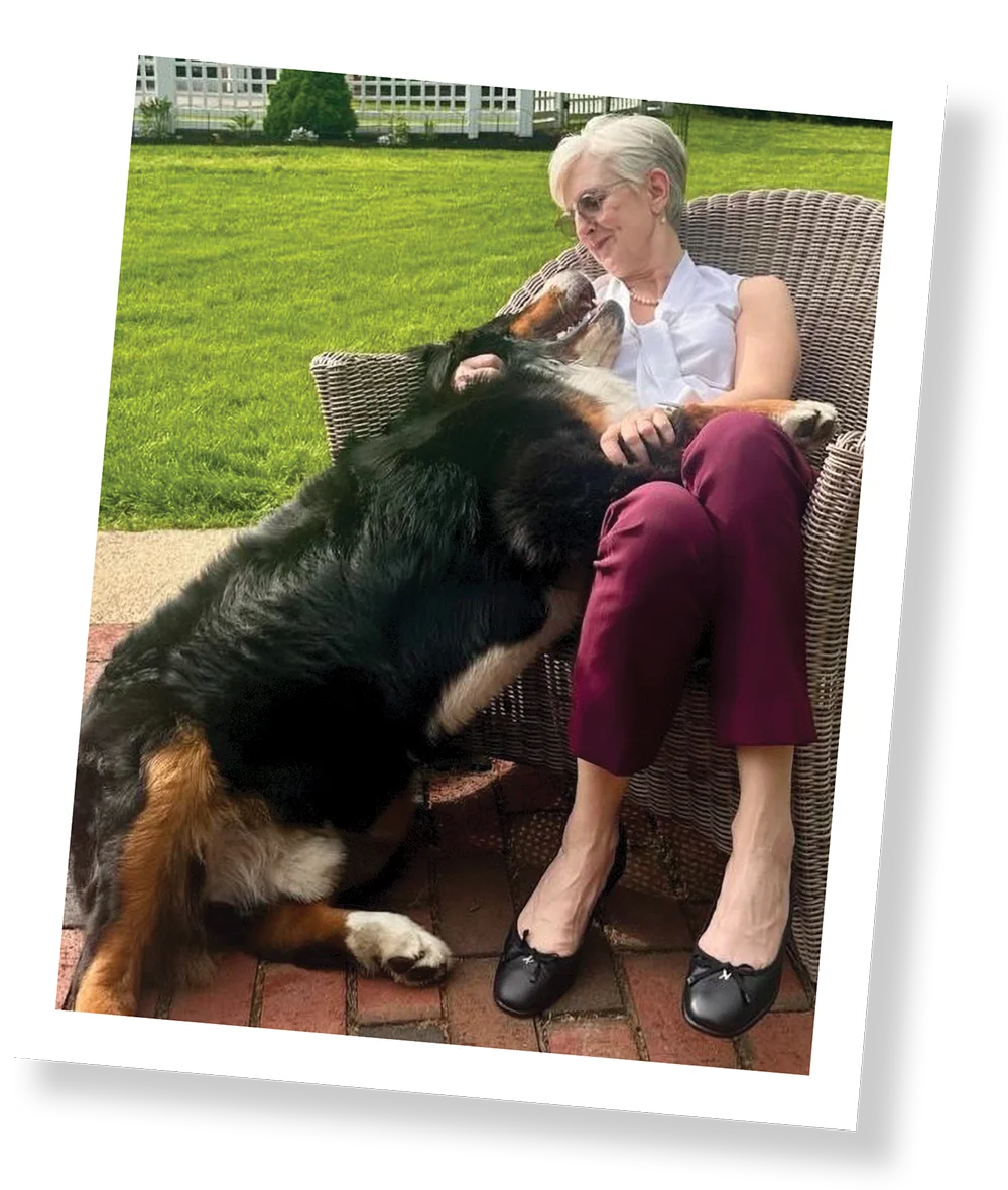 A person sitting on a woven chair outdoors, affectionately interacting with a large dog.