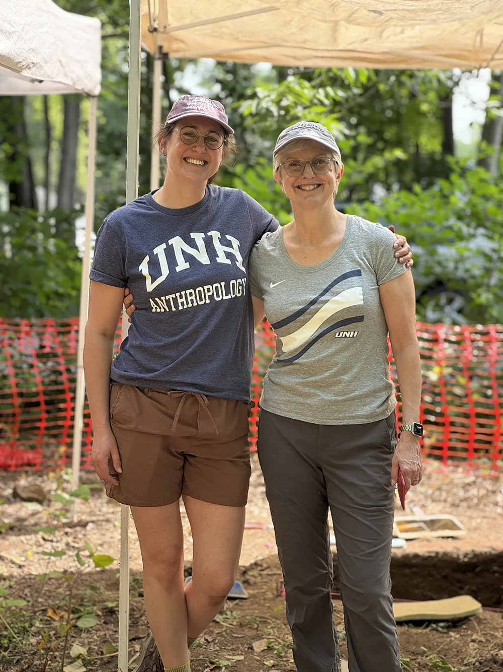 Two people smiling under a canopy tent outdoors, wearing "UNH" shirts.