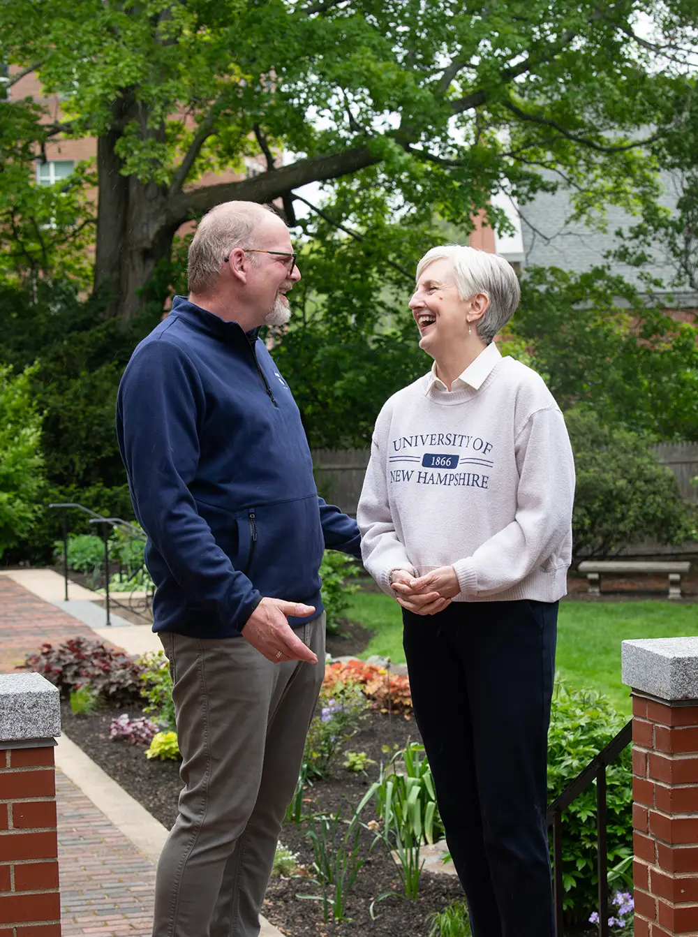 Two people talking in a garden, surrounded by greenery.