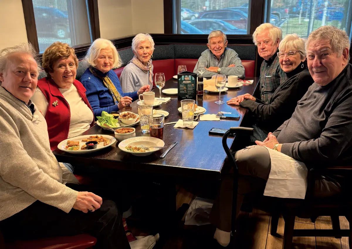 Photo of a gathering of 1961 University of New Hampshire grads in Concord in December inside at a restaurant table filled with food and other drinks, (pictured left to right): Marcus Johnson, Lois Magenau, Lise Tighe, Pam Monty, Art Monty, Bill Tighe, Pat D’Allesandro, Lou D’Allesandro