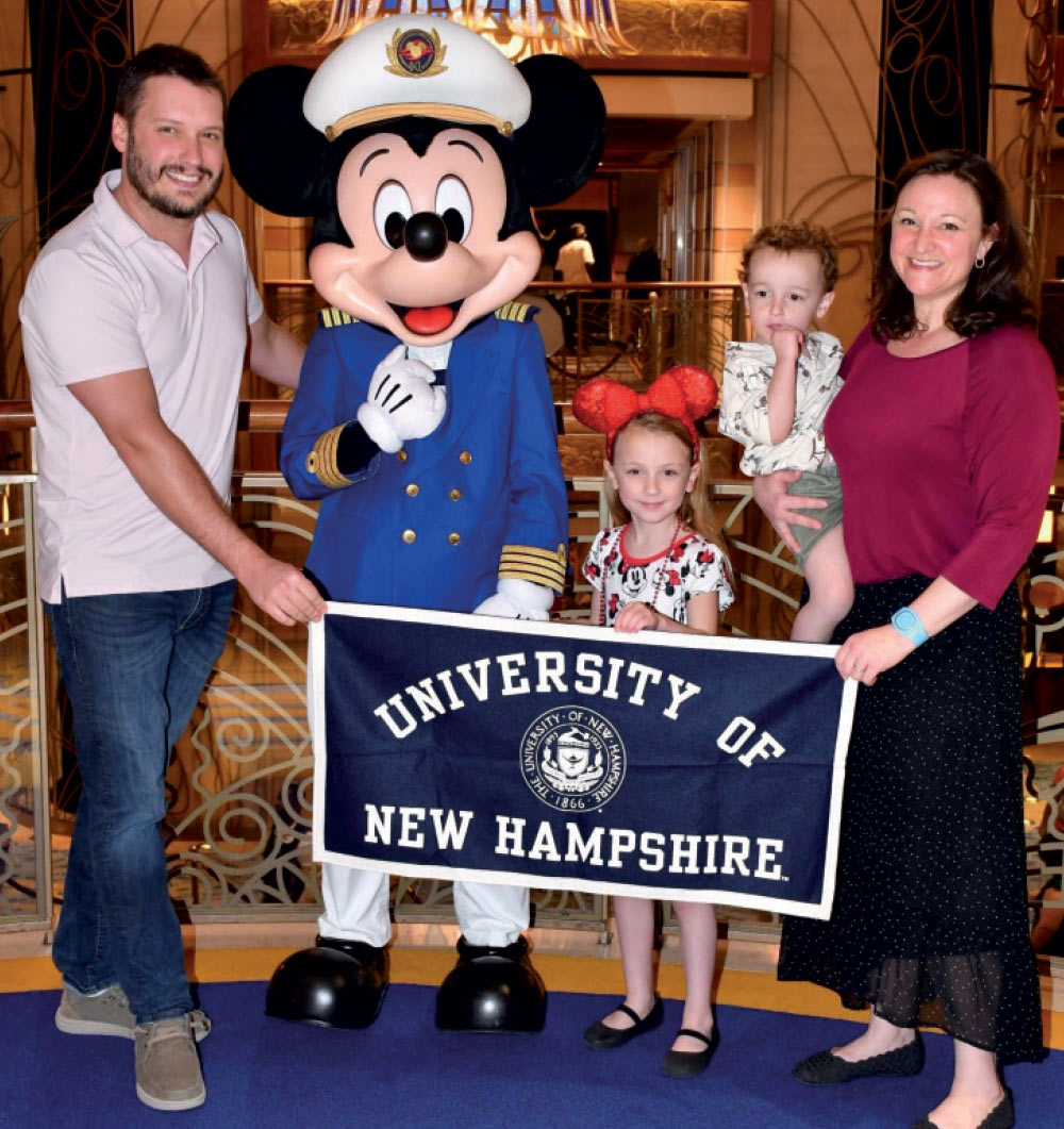 The Dittrich family posing for a photo with Mickey Mouse while holding a UNH banner 