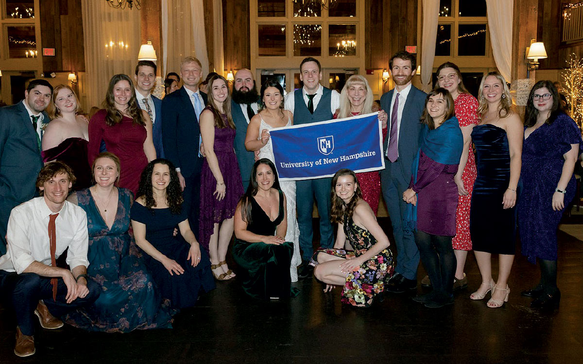 wedding party of Stephen Prescott ’14 ’21 and Katie Houde holding a UNH banner