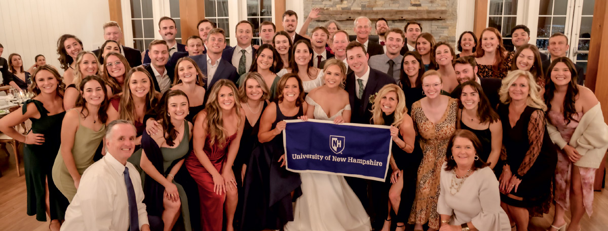 wedding party of Sarah Drake ’20 ’21G and Connor Smith ’19 holding a UNH banner
