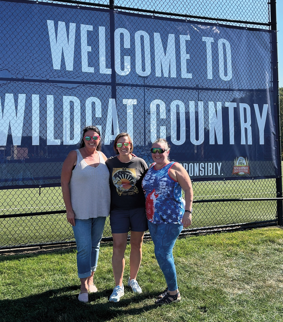 Homecoming pic of Liz Deering ’99, ’00G (daughter of Diane ’67 and David ’66 ’67G) who celebrated her 25th reunion at UNH Homecoming with Hetzel friends Lindsay Currier Walkinshaw ’00 and Rebecca Shost Harris ’00; Here the three women pose in front of a banner that reads WELCOME TO WILDCAT COUNTRY
