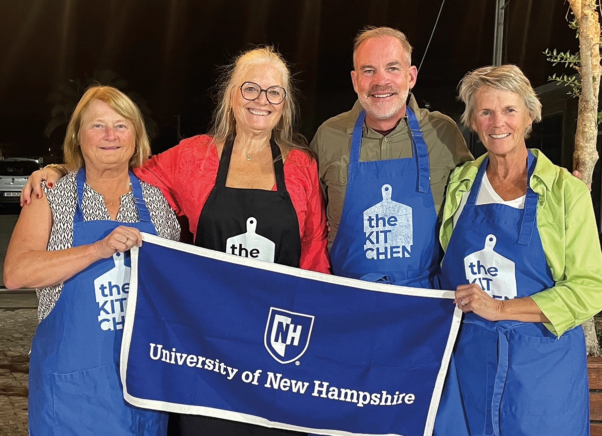 Deb Chase ’75, Eric Wasson ’88, ’92 and Caryl Dow ’80 are pictured with the mother of the owner of The KITCHEN in Lagos, Portugal; All these individuals are holding a University of New Hampshire banner of some kind