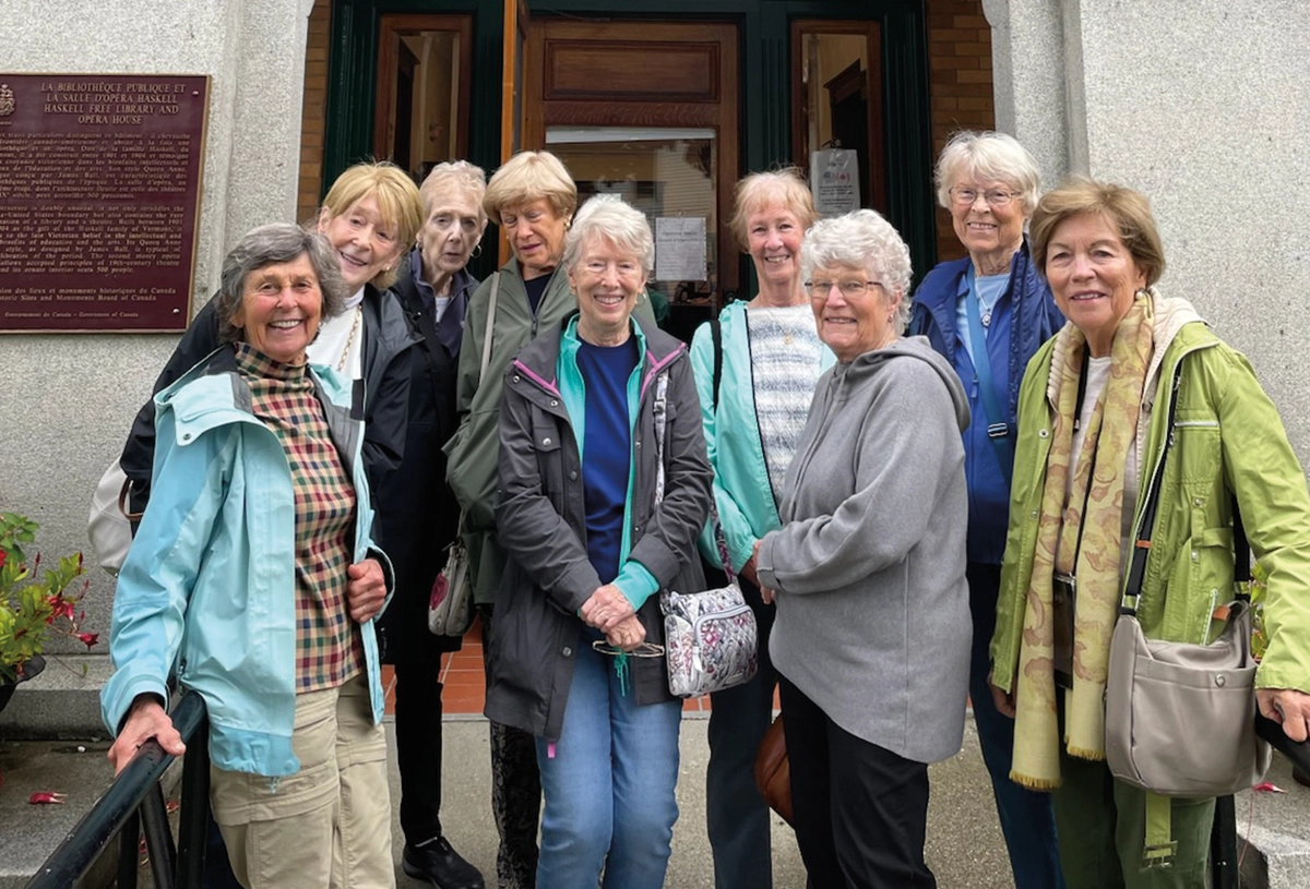The UNH ’64 Chi Omega gathering in summer 2025 in Vermont: Diane Chamberlain Philbrick, Mary Jayne Johnson Fischer-Haas, Ellie Walsh Swezey, Priscilla Wilde Burtt, Anne Thomson, Sally Hilton Eastwood, Frannie Mann Batchelder, Chris Riley Millar, Kathy Zegarra de la Pena; Here they are pictured all together smiling for a group photo next to each other nearby a building entrance of some kind