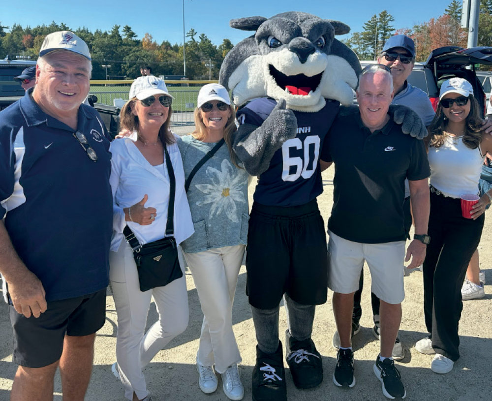A group of five people posing with the UNH Wildcats mascot, who is wearing a number 60 football jersey and giving a thumbs up.