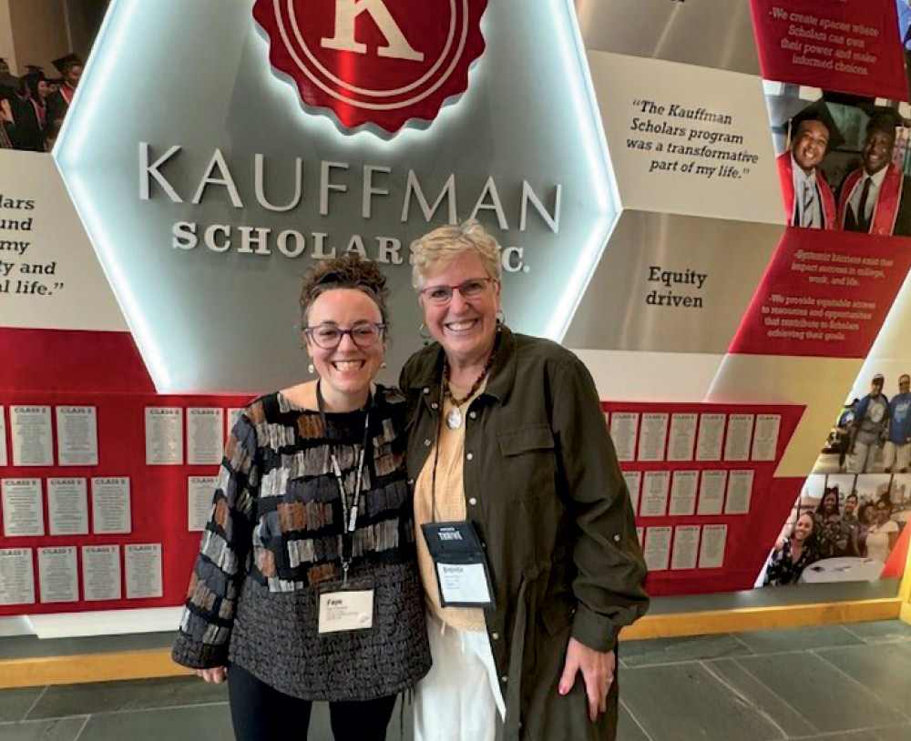 Two smiling women posing together in front of a large, illuminated "Kauffman Scholars Inc." wall display.