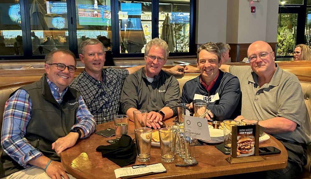 Five men sitting together at a circular wooden restaurant table with drinks and appetizers.
